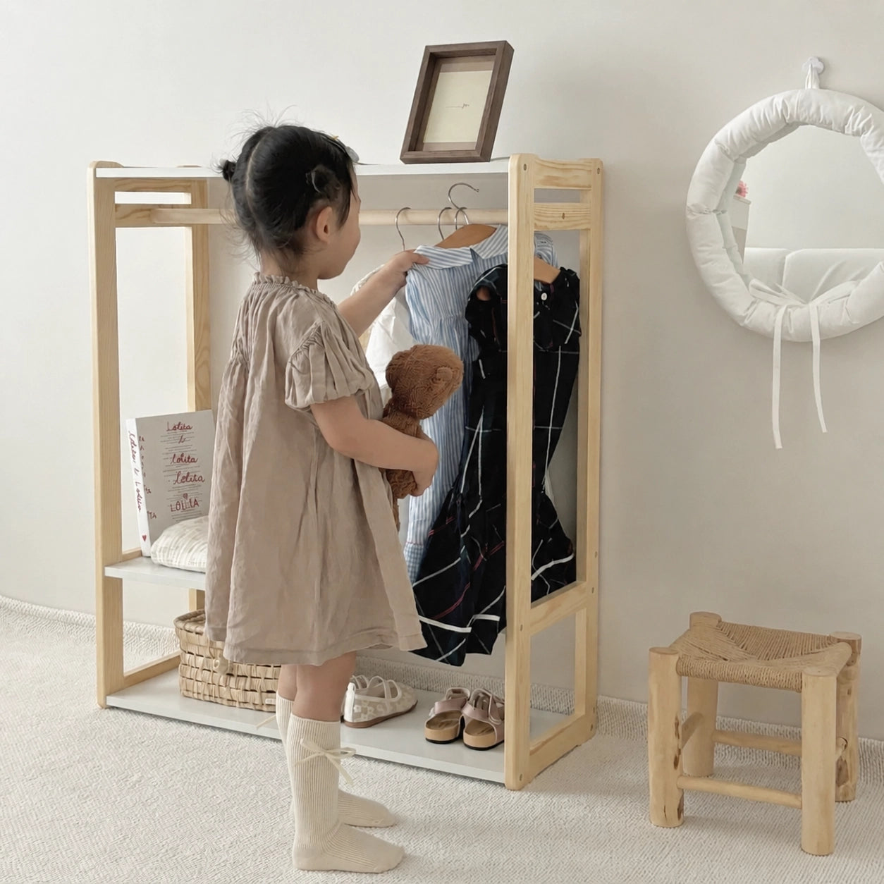 Angled view of a young child choosing dresses from a solid pine toddler wardrobe