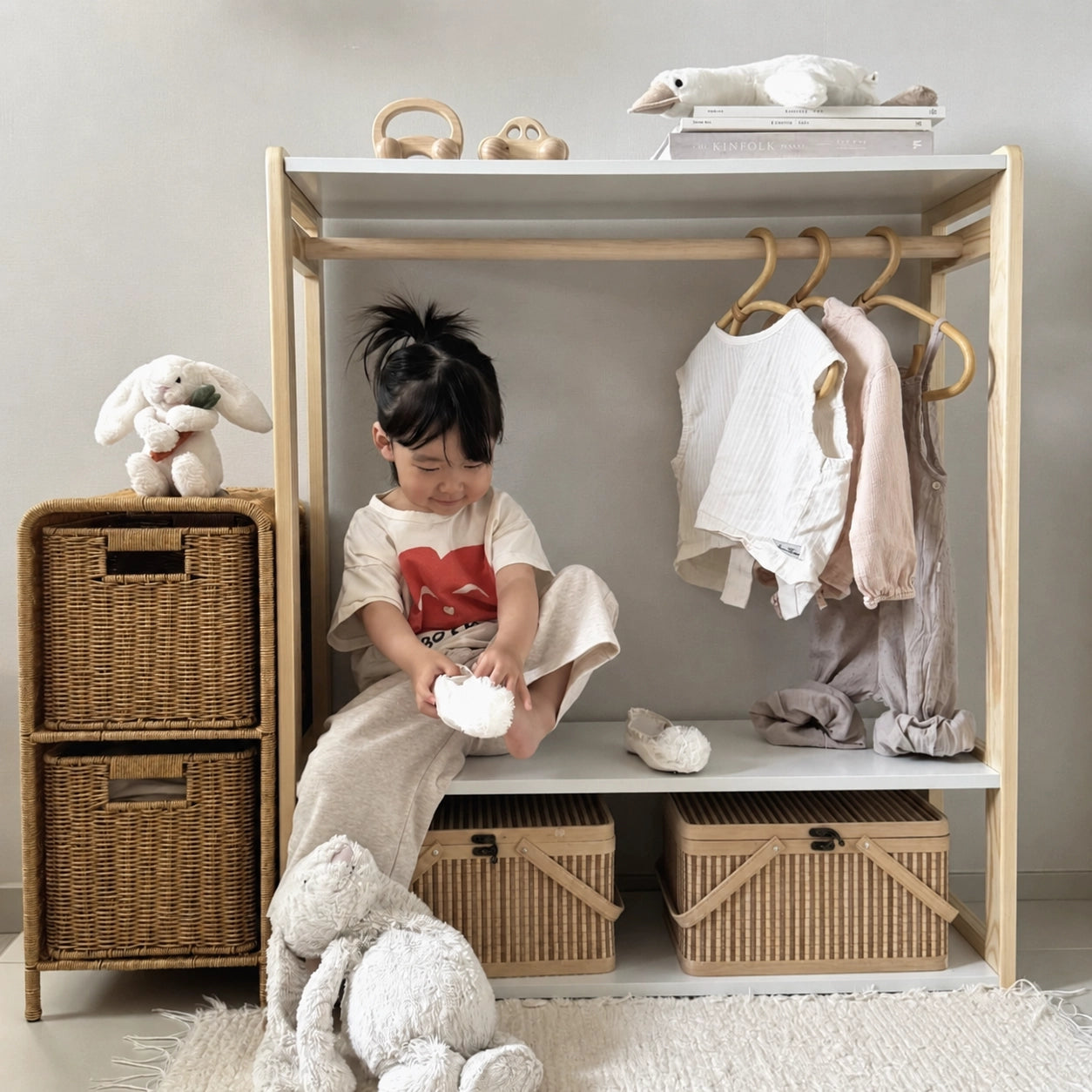 Young girl sitting on the shelf of a solid pine toddler wardrobe while putting on her shoes