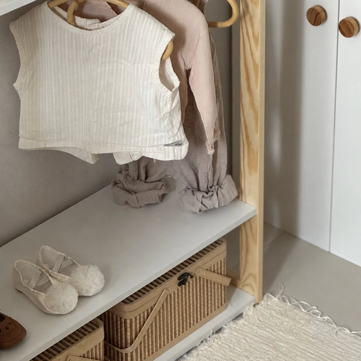 Detailed view of hanging kids clothes above a middle shelf with shoes and a woven storage basket