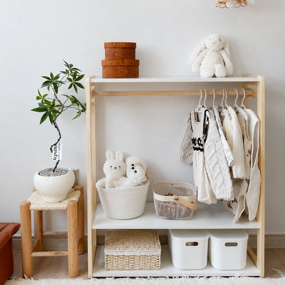 Solid pine toddler clothing rack with white storage bins on the lower shelf next to a potted plant